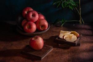 The apples on the plate look like oil paintings under the dim light on the wood grain table