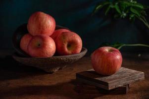 The apples on the plate look like oil paintings under the dim light on the wood grain table photo