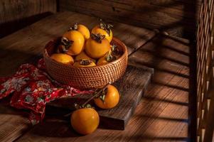 Persimmons on the plate are on the wooden table in dark light photo