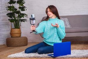 una hermosa joven se comunica con amigos en una conferencia en línea usando un teléfono y una computadora portátil. aprendizaje a distancia en cuarentena foto