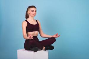 This girl is a fintes coach. She sits on a white cube and shows a relaxing lotus pose. The girl sits in the lotus position and meditates photo