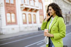 mujer joven usando un teléfono inteligente en la calle y sosteniendo café para llevar foto