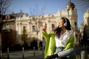Young woman listening music with smartphone on the street and holding takeaway coffee photo