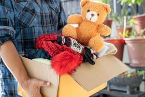 sosteniendo una caja de donación de ropa con ropa usada y muñecas en casa para apoyar la ayuda a los pobres del mundo. foto