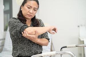 El paciente asiático de la mujer de la señora de mediana edad toca y siente dolor en el codo y el brazo, concepto médico sano. foto