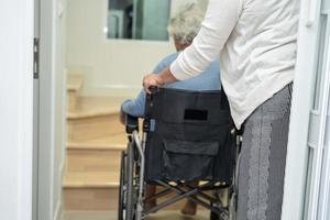 cuidador ayuda a anciana asiática o anciana sentada en silla de ruedas para subir las escaleras en casa. foto