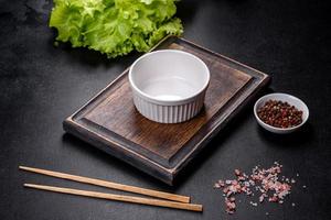 An empty white bowl and sticks on a wooden cutting board photo