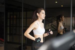 Beautiful asian sport woman is running on treadmill in the gym photo