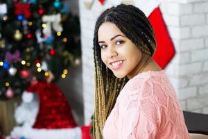 hermosa niña afroamericana de navidad se sienta en un fondo de decoraciones navideñas. foto