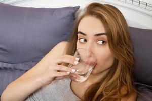Beautiful teen woman drinks water in the morning in bed close up.