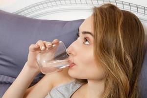 Beautiful girl drinks water in the morning in bed close up photo