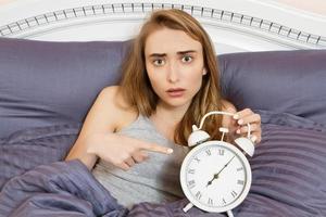 Shocked young woman waking up with alarm, girl point on clocks in bed photo