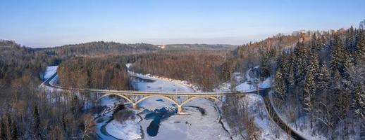 Aerial view of the river and snow-covered forest after a blizzard in a morning haze. Clear blue sky. Winter wonderland. Gauja national park, Sigulda, Latvia photo