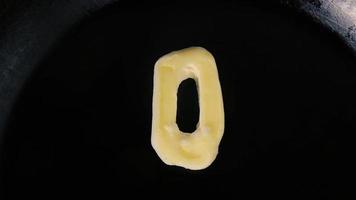 Butter in shape of number 0 melting on hot pan - Close up top view video