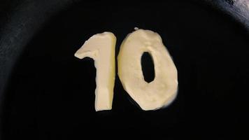 Butter in shape of number 10 melting on hot pan - Close up top view video