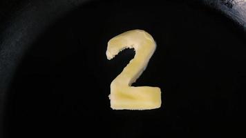 Butter in shape of number 2 melting on hot pan - Close up top view video