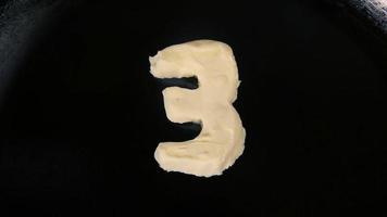mantequilla en forma de número 3 derritiéndose en una sartén caliente - vista superior de cerca video