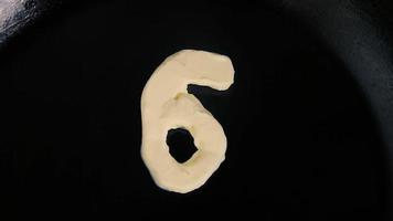 Butter in shape of number 6 melting on hot pan - Close up top view video