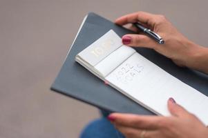 Black woman with red nail polish writing her new year's resolution in a to do list notebook with a black pen photo