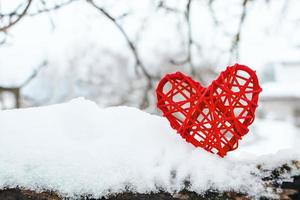 Wooden red heart on background of snow-covered tree branches. Eco-friendly valentines day.