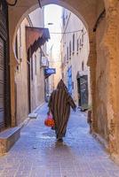 Rear view of man walking in traditional hood clothing while carrying oranges photo