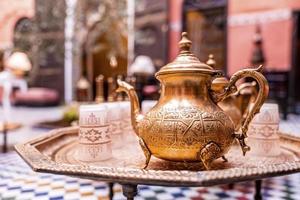 Traditional ornate copper teapot with glasses on table photo