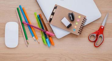 concepto de regreso a la escuela con útiles escolares, computadora portátil, libro, bolígrafo, mouse y lápiz de color sobre una mesa de madera. foto