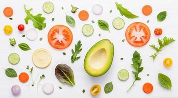Food pattern with raw ingredients of salad, lettuce leaves, cucumbers, tomatoes, carrots, broccoli, basil ,onion and lemon flat lay on white wooden background. photo
