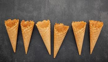 Colección de conos de helado planos laicos sobre fondo de piedra oscura. Cono de helado crujiente en blanco con espacio de copia para el diseño del menú de dulces. foto