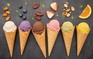 varios sabores de helado en conos de arándano, pistacho, almendra, naranja y chocolate sobre fondo de piedra oscura. concepto de menú de verano y dulce. foto