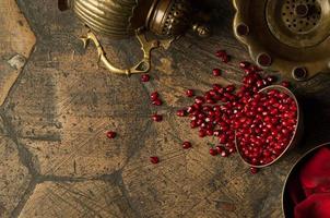 granos y semillas de granada con una jarra de cobre sobre un antiguo adoquín decorativo. Jarra de cobre antiguo con una granada sobre un azulejo antiguo foto