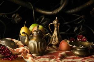 fruit and a metal jug with bowls in oriental style on the background of decorative forging ornament. still life in oriental style photo
