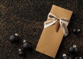 folleto de regalo con adornos para árboles de Navidad sobre un fondo dorado granulado. Folleto con cinta sobre un fondo granulado dorado negro