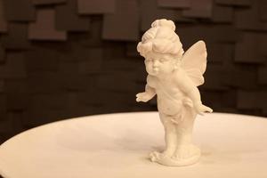 estatua de una niña ángel con alas en un plato blanco sobre un fondo oscuro foto