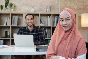 Retrato de empresario de inicio de negocios, joven y bella propietaria, dos socios islámicos, mirando a cámara, sonríe felizmente en la pequeña oficina de trabajo de comercio electrónico.