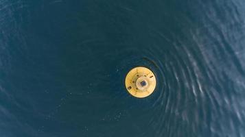 Aerial photo of yellow buoy bobbing in deep water making ripples and waves