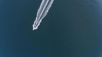 Aerial photo of small boat with white waves in wake on deep blue water