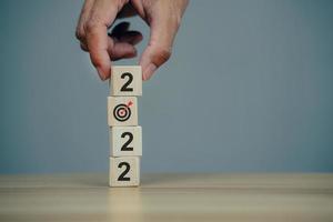 Businessman hand holding woods cube with new year icon word 2022 and goal target icon. photo