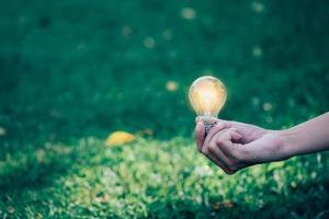 Closeup hand man hold light bulb on green nature background photo