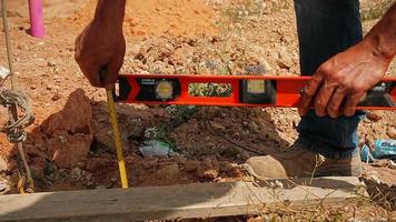trabalhador da construção civil verificando a profundidade do buraco em um canteiro de obras com um nível de bolha e uma fita métrica video