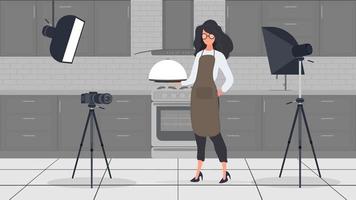 Woman cook in the kitchen leads a culinary vlog. A girl in a kitchen apron holds a metal tray with a round lid. Vector.