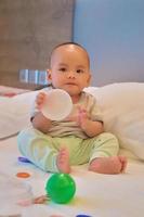 retrato de un feliz bebé asiático de 6 meses sentado en la cama jugando foto