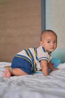 retrato de un pequeño y feliz bebé asiático de 6 meses sentado en la cama en casa