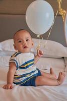 Portrait of happy 6 month old Asian baby boy sitting on bed playing
