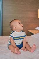 retrato de un pequeño y feliz bebé asiático de 6 meses sentado en la cama en casa