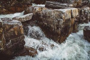 Stream of river among stones and rocks. Stream in stone bed, fast mountain river among rocks, water boils in eddies of current photo