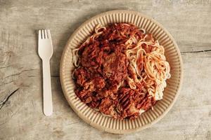 Spaghetti bolognese pasta with tomato sauce and minced meat on rustic wooden background. Wooden fork and paper plate. Eco friendly disposable tableware. Top view. Copy, empty space for text photo