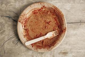 Dirty from food disposable paper utensils on a wooden background. Wooden fork and paper plate on wooden background. Eco friendly disposable tableware. Top view. Copy, empty space for text photo