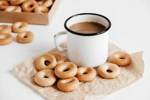Metal mug with hot drink and mini round bagels on a white wooden background. Copy, empty space for text photo