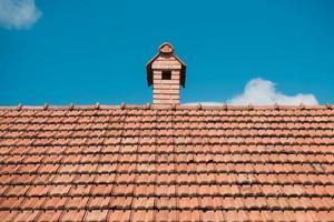 Old roof tiles on the roof of an house with chimney on sky background. Place for text or advertising photo